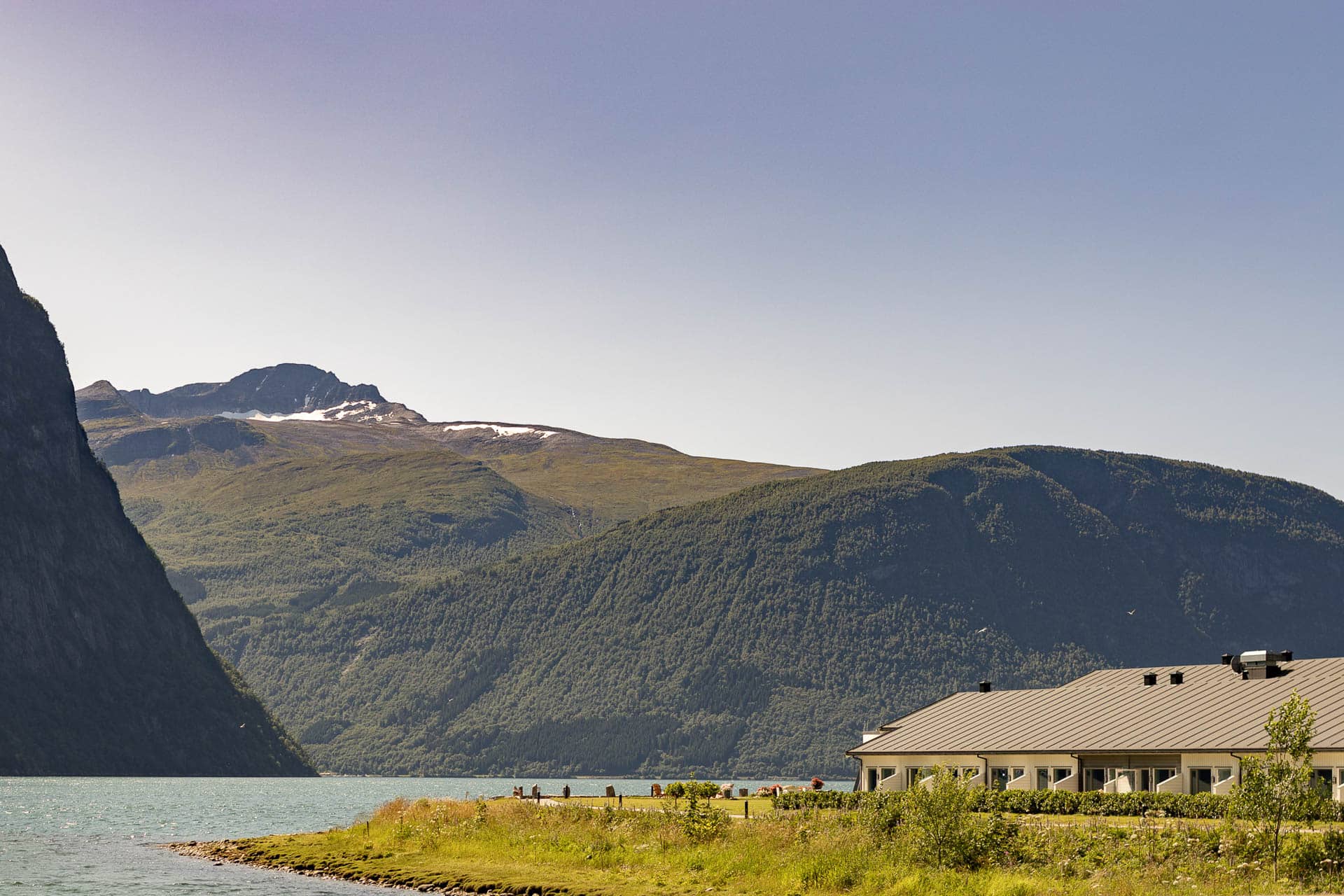 Valldal Fjordhotell ved fjorden med grønne fjell i bakgrunnen